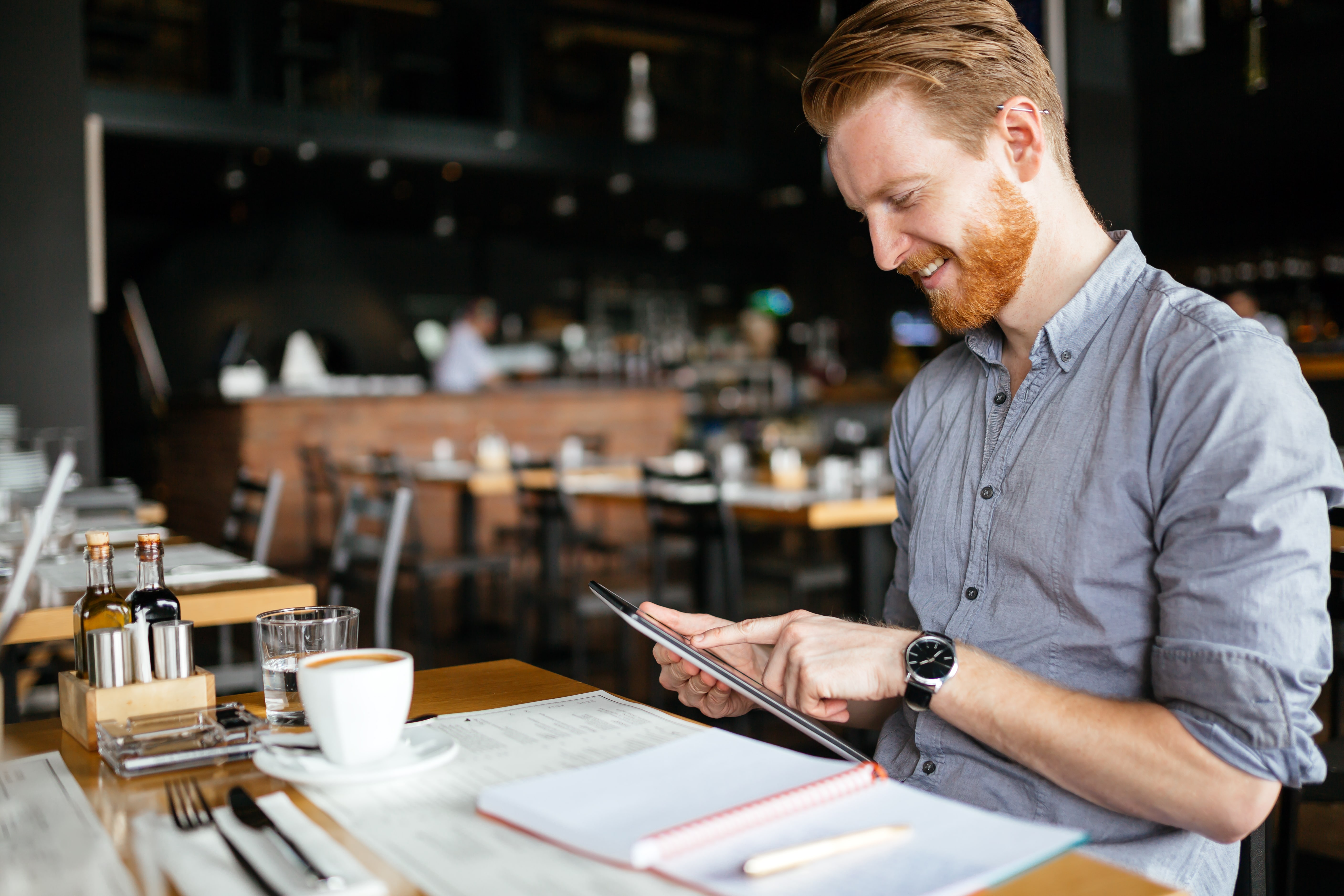 Happy man smiling whilst working on his iPad in a café.